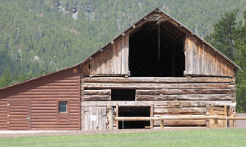 A rustic wooden barn set against a backdrop of trees and a hillside.