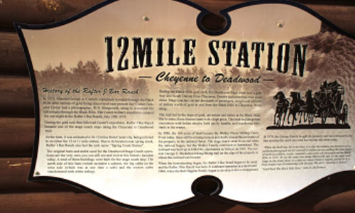 Historical sign titled "12 Mile Station" with text and stagecoach illustration.