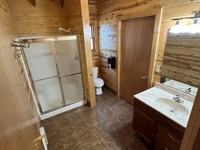 Wood-paneled bathroom with shower, toilet, and sink on tiled floor.