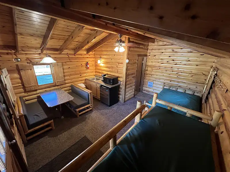 Cozy wooden cabin interior with a seating area, small kitchen, and lofted bed.