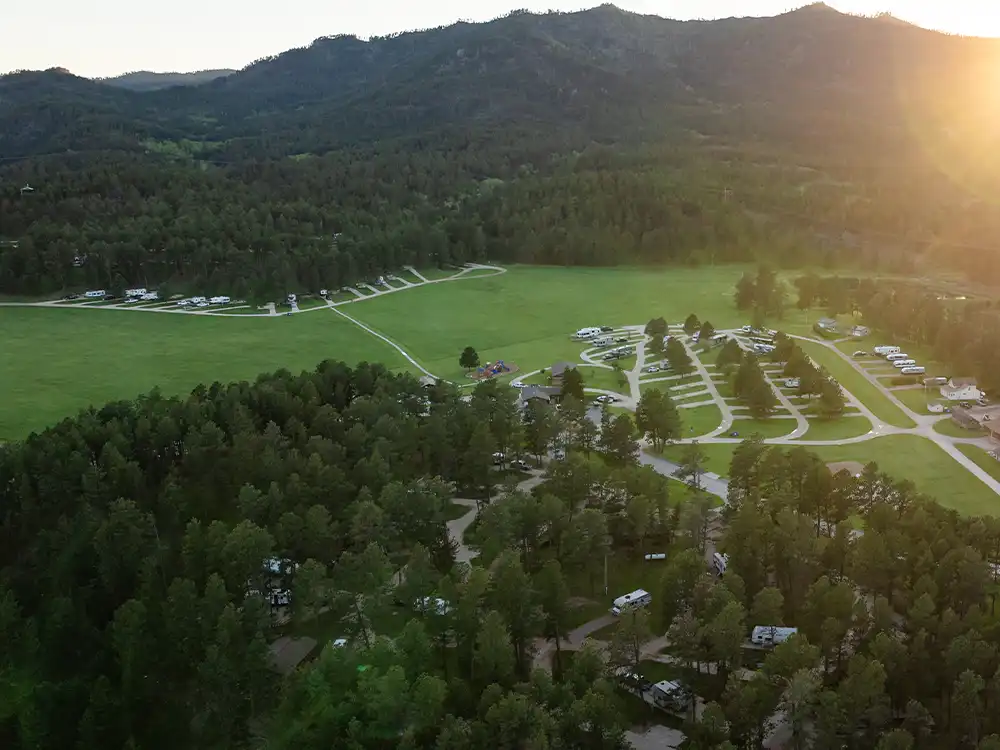 Aerial view of Black Hills Campground with RVs and tents nestled near a forested area at sunset.