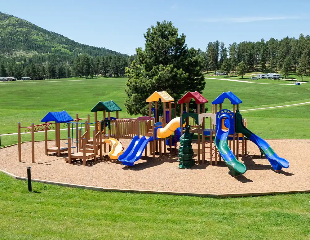 A colorful playground with slides and climbing structures on a grassy field near trees.